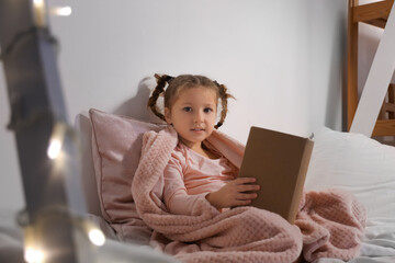 Cute little girl reading story in bedroom at night