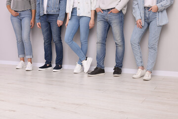 Group of people in stylish jeans near light grey wall indoors, closeup