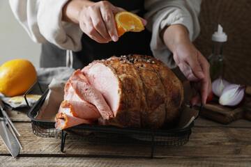 Woman squeezing juice from orange slice onto delicious baked ham at wooden table, closeup