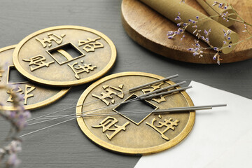 Acupuncture needles, moxa sticks and antique Chinese coins on grey wooden table, closeup