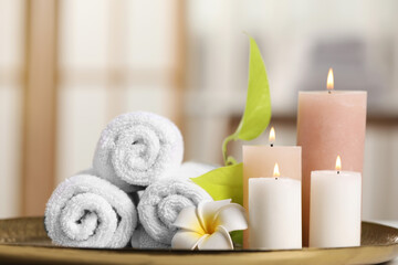 Fototapeta na wymiar Spa composition. Burning candles, plumeria flower, green leaves and towels on tray