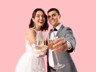 Young wedding couple with glasses of champagne on pink background