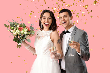 Young wedding couple with bouquet of flowers and champagne on pink background