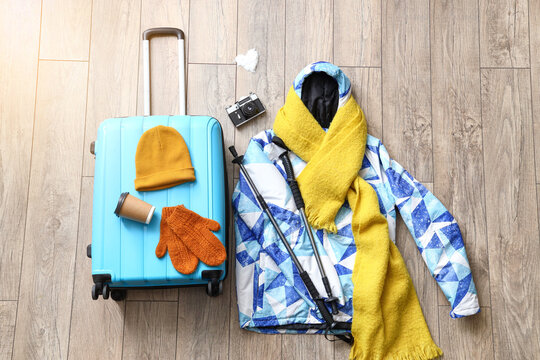 Composition with warm clothes, suitcase and walking poles on wooden floor