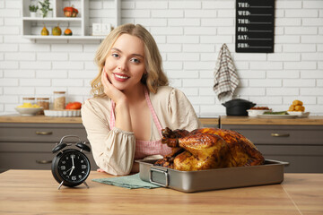 Beautiful young woman with tasty baked turkey and alarm clock at table in kitchen. Thanksgiving Day celebration
