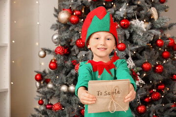 Cute little boy in elf costume with letters to Santa at home on Christmas eve