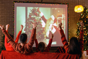 Happy family watching Christmas movie on projector screen at home, back view - obrazy, fototapety, plakaty