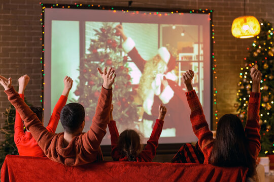 Happy Family Watching Christmas Movie On Projector Screen At Home, Back View