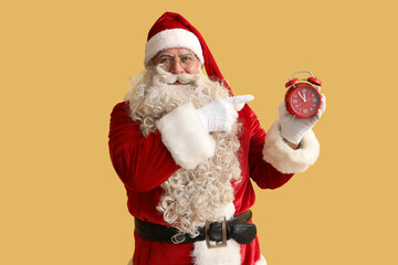 Fototapeta na wymiar Santa Claus pointing at alarm clock on yellow background