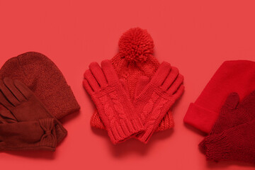 Set of warm gloves and hats on red background