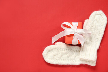 Fototapeta na wymiar Warm mittens and Christmas gift on red background
