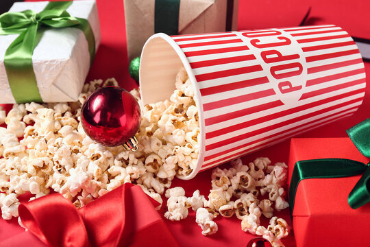 Bucket of popcorn with Christmas balls and gifts on red background
