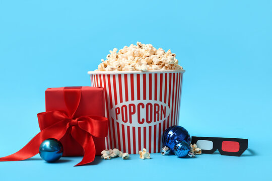 Bucket of popcorn with 3D glasses, gift box and Christmas balls on blue background