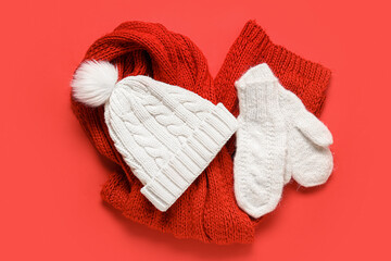 Pair of white knitted mittens with warm hat and scarf on red background
