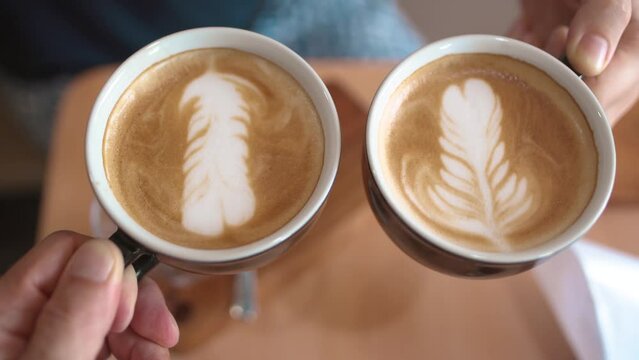 Close-up of two cups of fresh brewed cappuccino coffee with milk foam are held in the hands of two people. Top-down view.