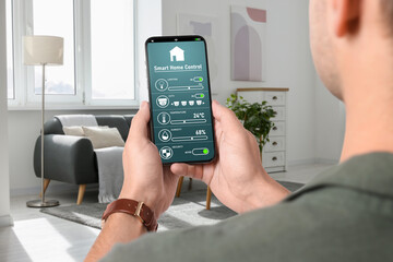 Man using smart home control system via application on mobile phone indoors, closeup - obrazy, fototapety, plakaty