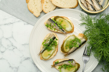 Delicious sandwiches with sprats, pickled cucumber, green onion and dill served on white marble table, flat lay. Space for text
