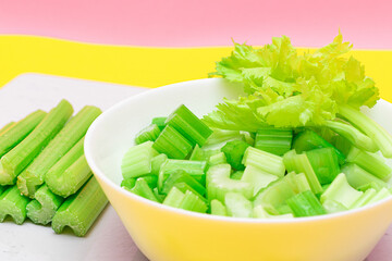 Fresh Chopped Celery Slices in White Bowl with Celery Sticks on White Cutting Board. Vegan and Vegetarian Culture. Raw Food. Healthy Diet with Negative Calorie Content