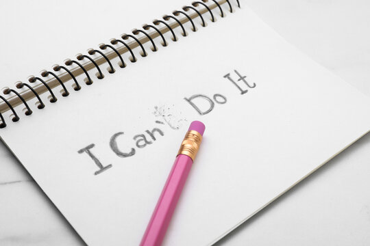 Motivation concept. Notebook with changed phrase from I Can't Do It into I Can Do It by erasing letter T on white table