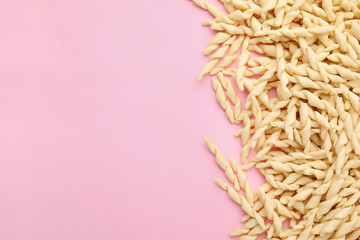 Uncooked trofie pasta on pink background, flat lay. Space for text