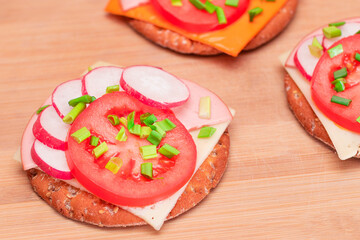 Crispy Cracker Sandwiches with Tomato, Sausage, Cheese, Green Onions and Radish on Cutting Board....