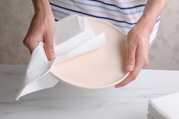 Woman wiping plate with tissue paper at white marble table, closeup - obrazy, fototapety, plakaty