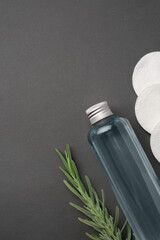 Bottle of makeup remover, cotton pads and rosemary on dark grey background, flat lay. Space for text