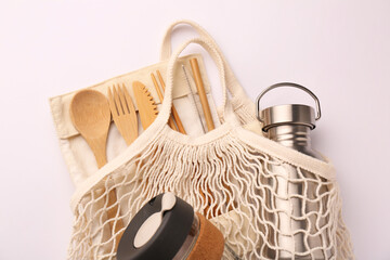 Fishnet bag with different items on white background, top view. Conscious consumption