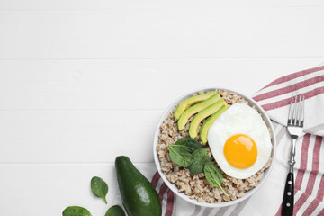 Tasty boiled oatmeal with fried egg, avocado and basil served on white wooden table, flat lay. Space for text