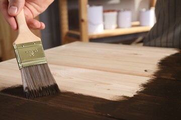 Man with brush applying wood stain onto wooden surface indoors, closeup