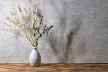 Background with bouquet of dried plants in vase. Wooden background. Sunset light.