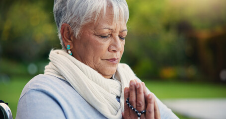 Senior woman, praying hands or rosary in wheelchair in nature, faith or hope in retirement. Mature...