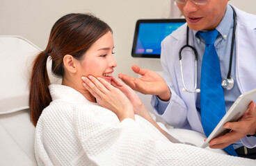 young attractive asian woman lying on couch in beauty clinic,smiling and talking with a doctor that consulting her for doing aesthetic procedure with a tablet computer,concept of health and aesthetic