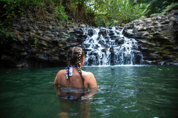 Rear view of a woman swimming in a relaxing waterfall pool. Active, fit Woman with pony tails taking a refreshing swim in a scenic tropical destination
