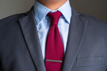 Burgundy knitted necktie is tied in four-in-hand knot with single dimple and tie clip pairing...