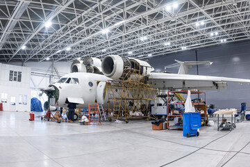 White transport aircraft in the aviation hangar. Airplane under maintenance. Checking mechanical systems for flight operations - obrazy, fototapety, plakaty
