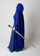 Full length portrait of beautiful female model wearing elegant fantasy blue ball gown, flowing cape...