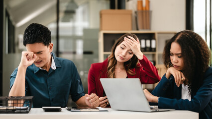 Fototapeta na wymiar Business team meeting with stressed man rubbing his forehead, while two women review documents, appearing serious and focused.
