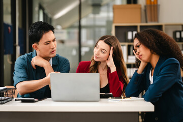 Business team meeting with stressed man rubbing his forehead, while two women review documents, appearing serious and focused.