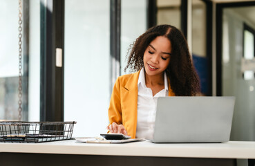 African American businesswoman, focused on her work on a laptop, possibly managing industrial...