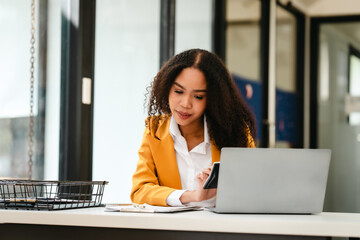 African American businesswoman, focused on her work on a laptop, possibly managing industrial...