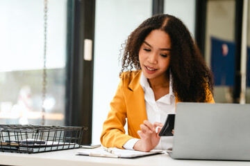 African American businesswoman, focused on her work on a laptop, possibly managing industrial...
