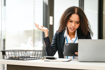 African American businesswoman, focused on her work on a laptop, possibly managing industrial...