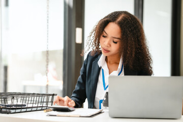 African American businesswoman, focused on her work on a laptop, possibly managing industrial...