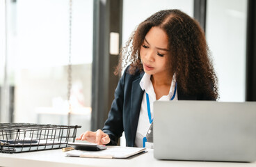African American businesswoman, focused on her work on a laptop, possibly managing industrial...