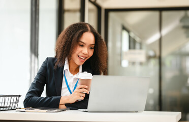 African American businesswoman, focused on her work on a laptop, possibly managing industrial production tasks.