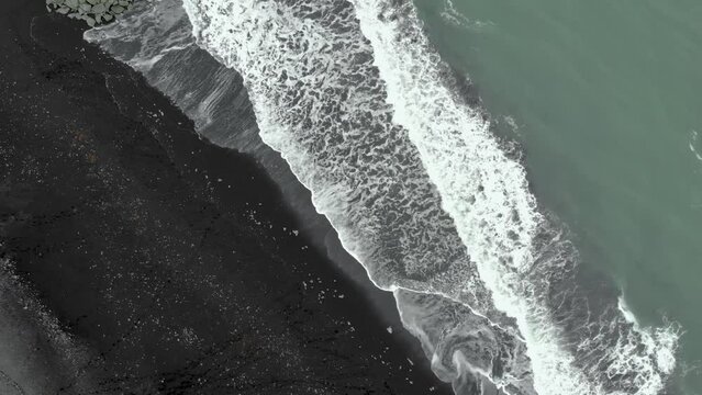 Top down aerial pan of Diamond Beach in Iceland, where waves put ice on the black sand.