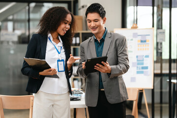 Confident Asian businessman and African American businesswoman reviewing and discussing UX/UI design elements together at desk. in formal suit