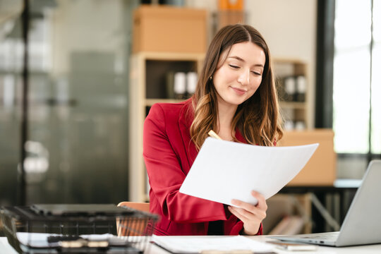 Caucasian businesswoman, likely an accountant or CPA, smiling and holding a coffee cup while working on her laptop.