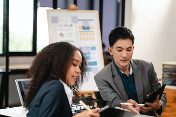 Confident Asian businessman and African American businesswoman reviewing and discussing UX/UI design elements together at desk. in formal suit